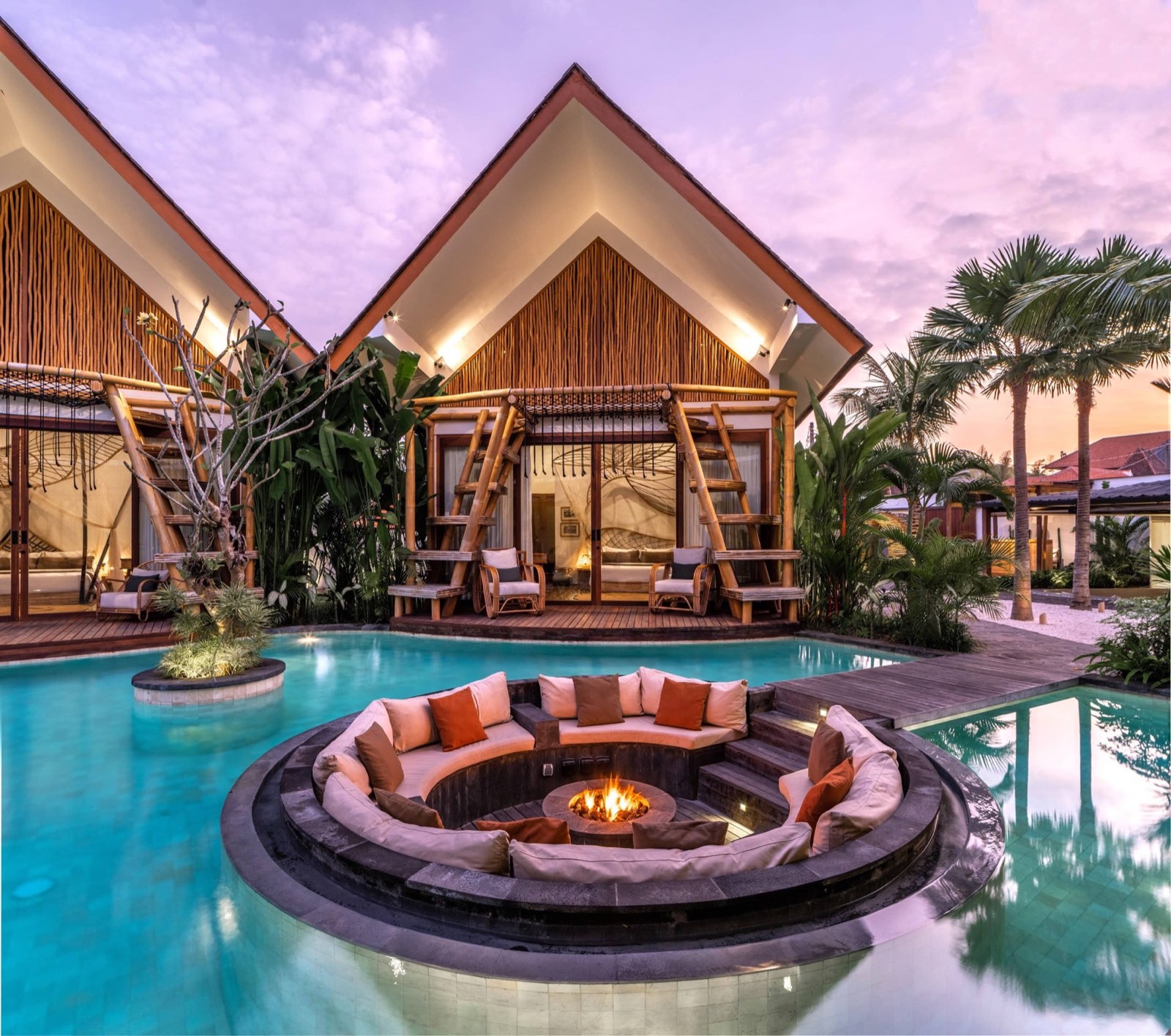 Sunken fire pit in the pool at dusk, with timber villas behind